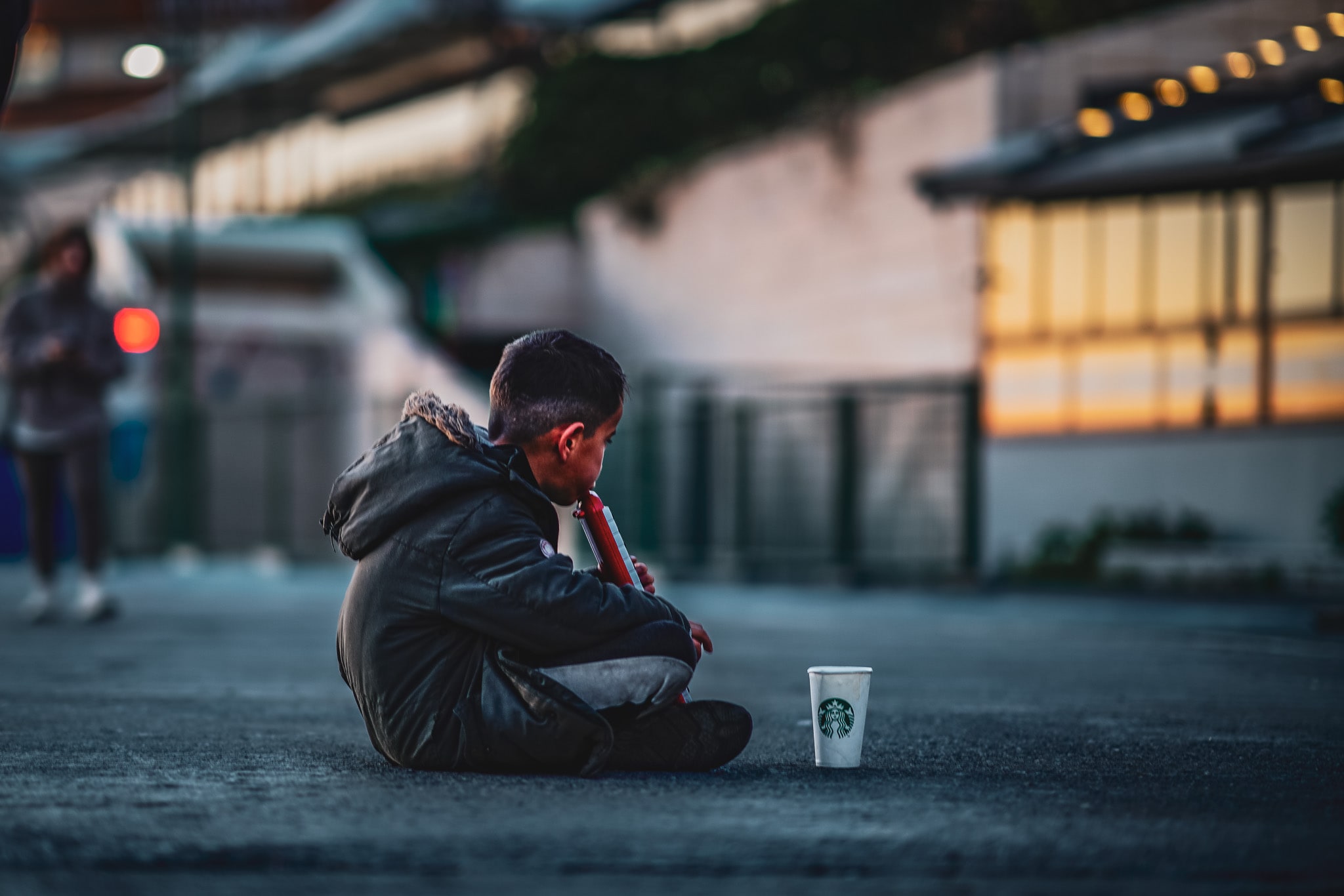 A solitary man sitting beside a paper cup on a city street