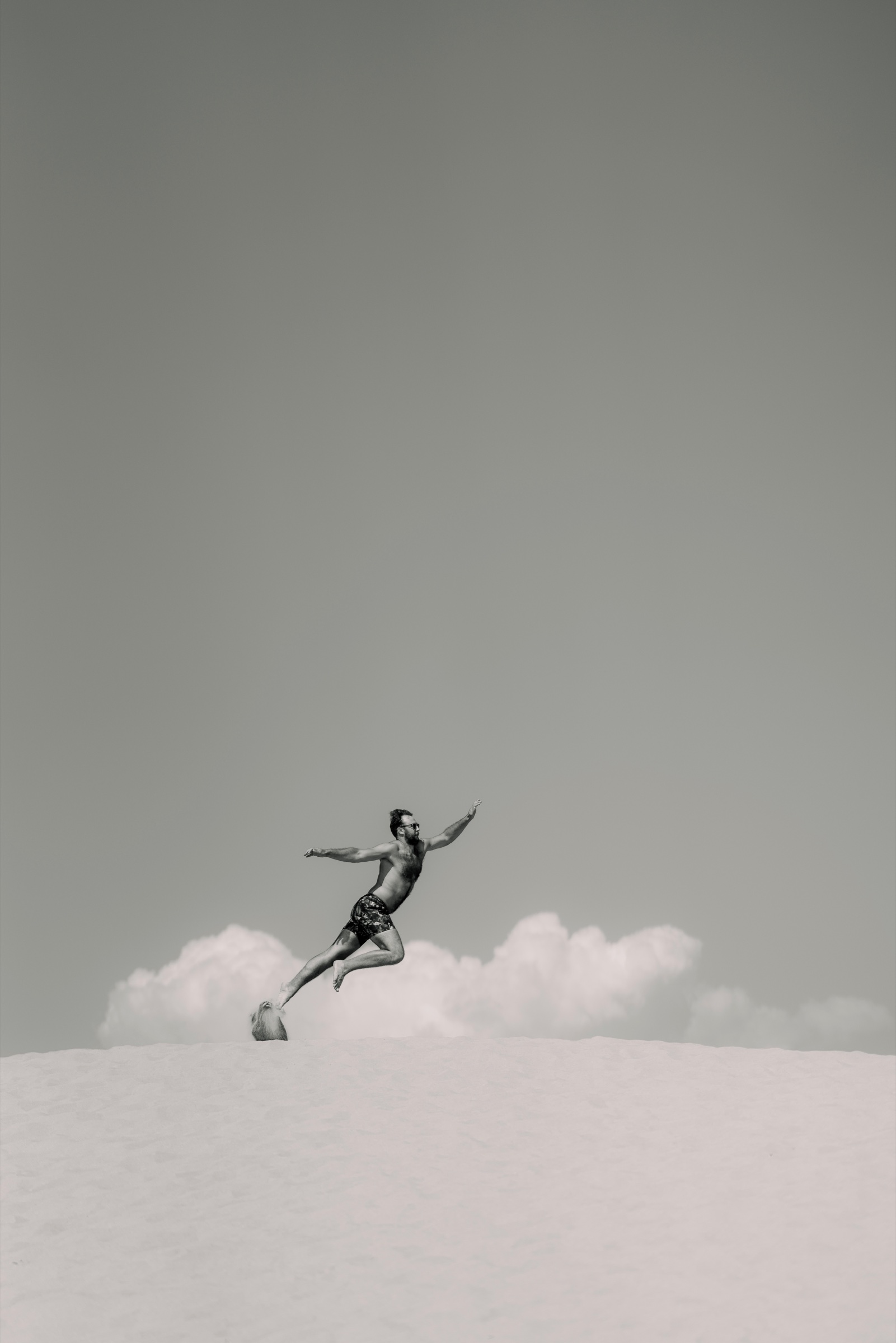 Black-and-white figure suspended above a pale beach