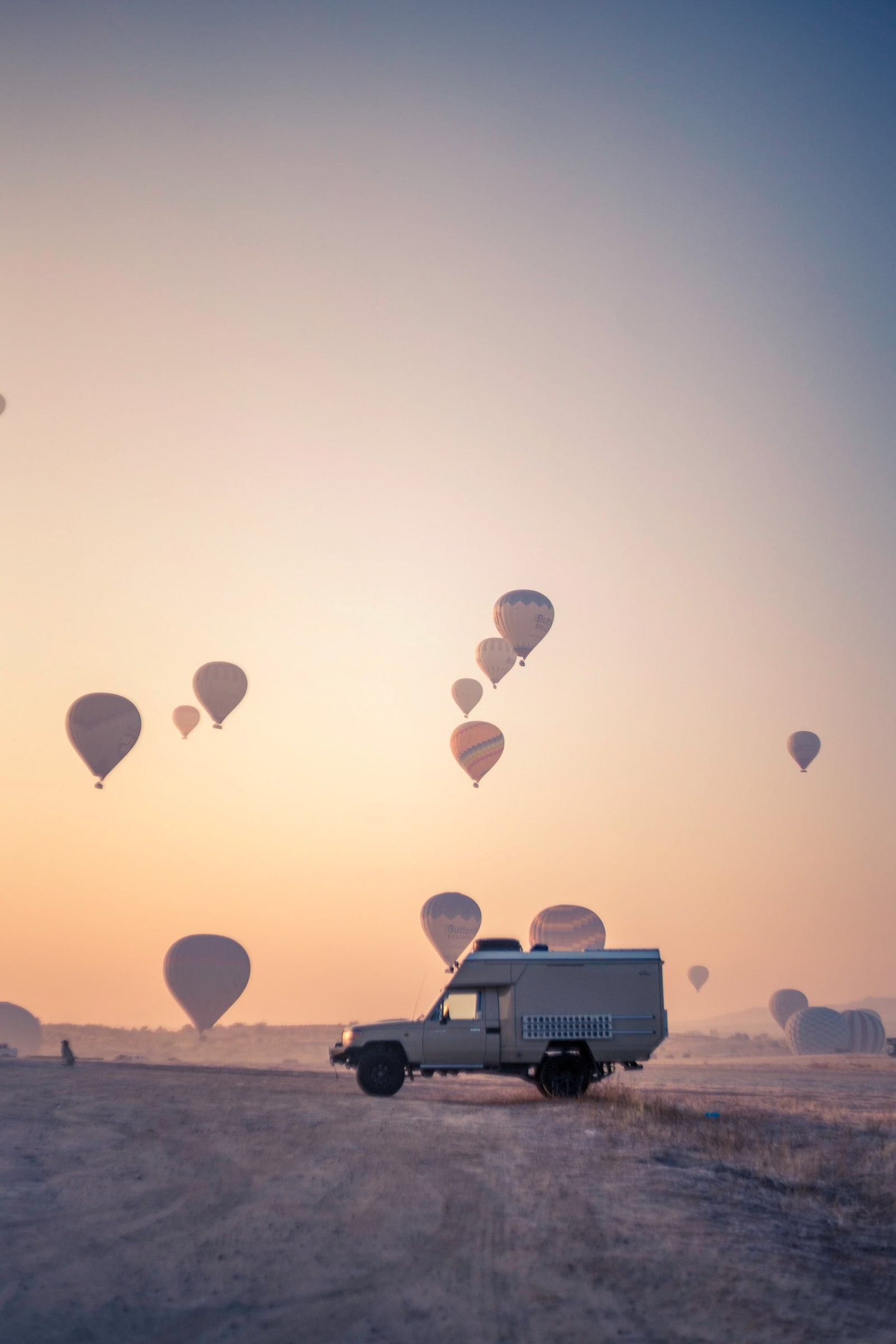 Hot-air balloons rising at dawn beside a vehicle in the desert