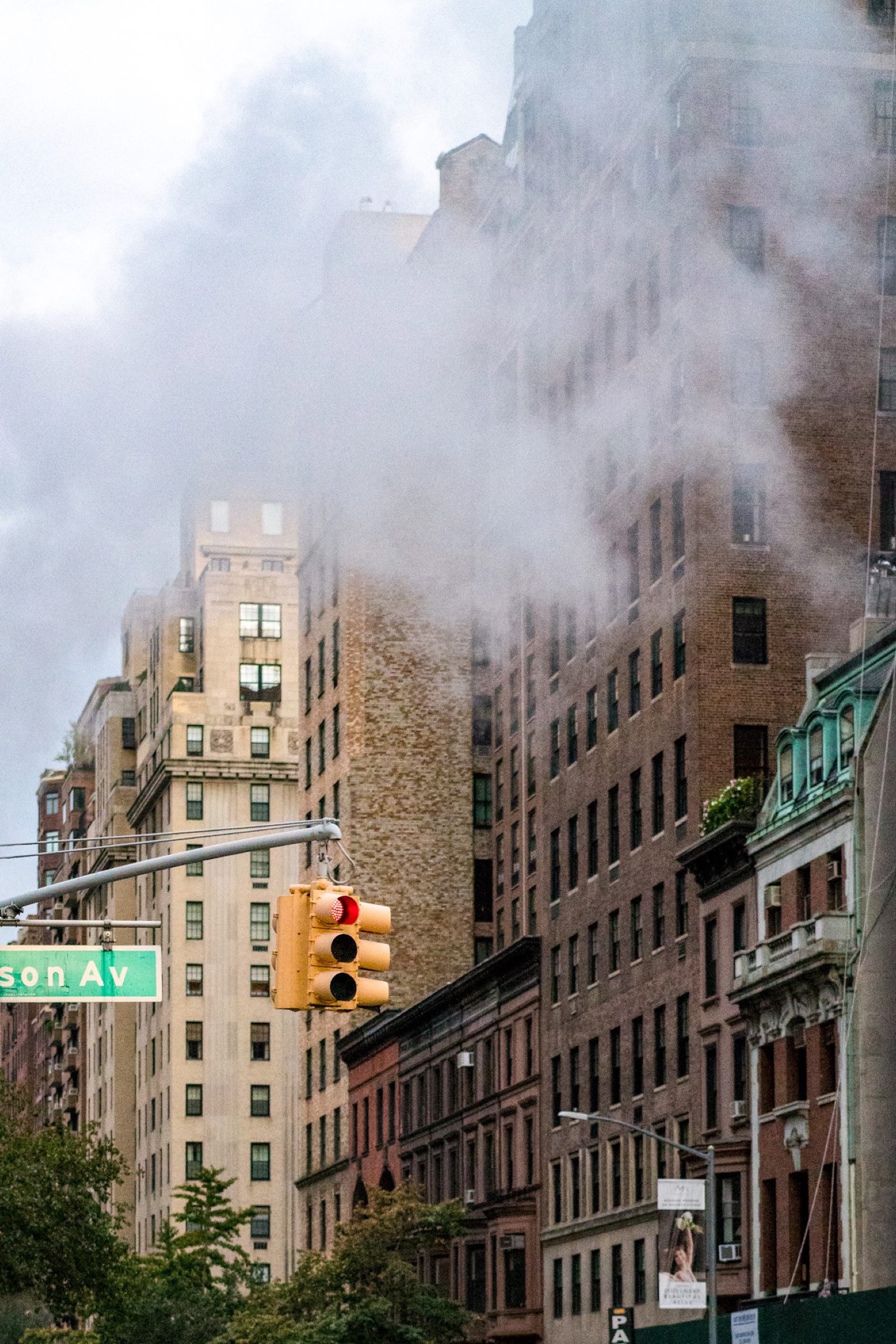 Steam rising between Manhattan buildings above a red traffic light