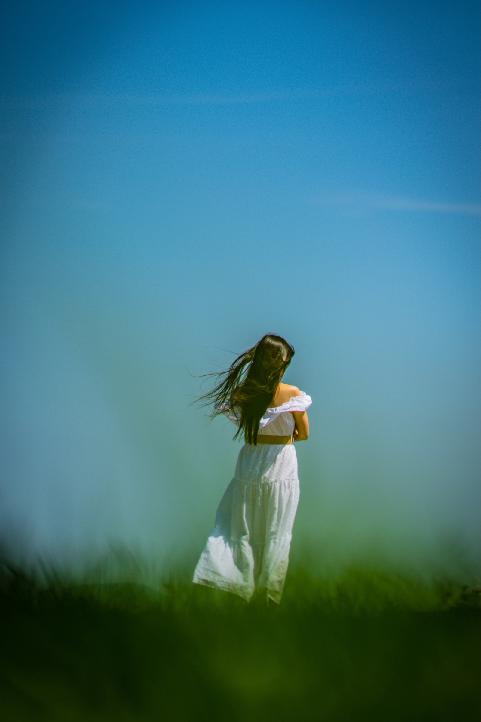 Woman in a white dress standing in an open blue and green landscape