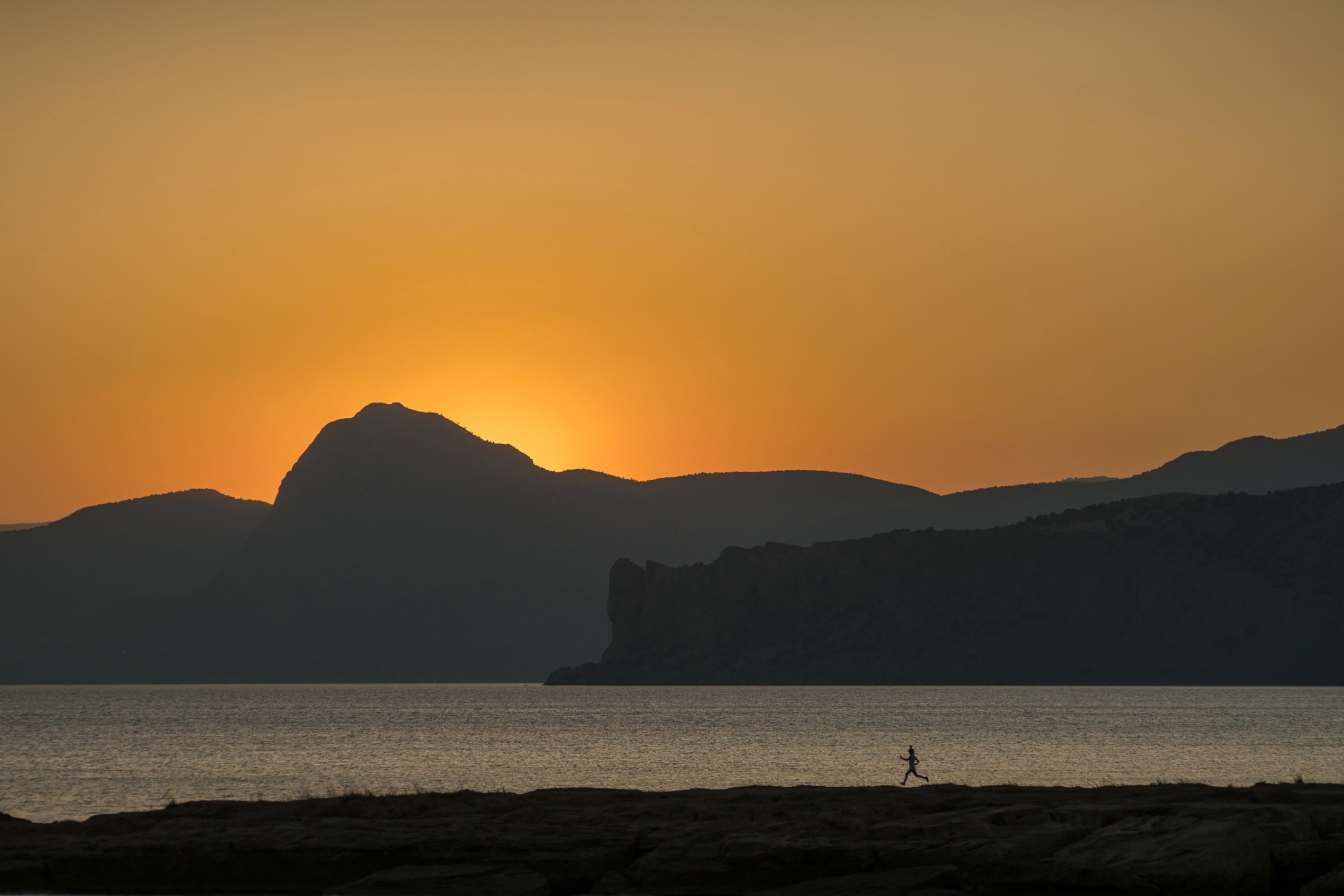Runner silhouetted against a sunset over the sea